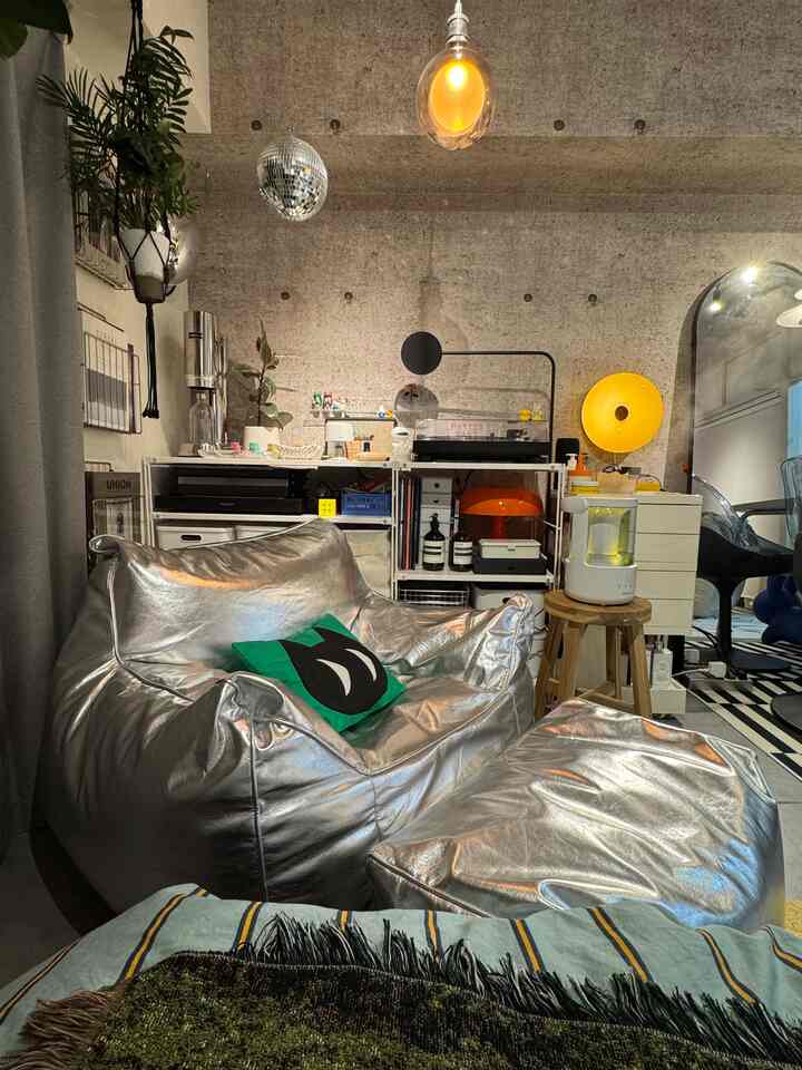 Modern small room featuring silver bean bag sofa and ottoman, with various lighting fixtures and shelves creating a cozy atmosphere