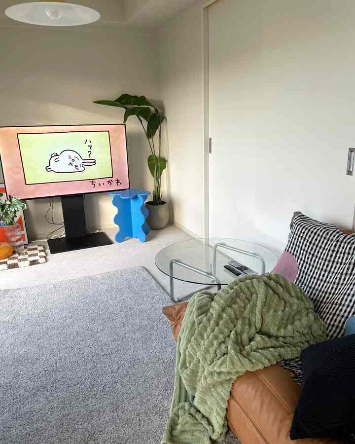 Compact living room with white walls and brown leather sofa, accented by a green throw and blue side table in a minimal setting
