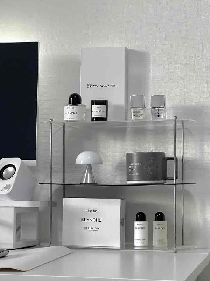 白と透明素材のシンプルなホームオフィスのデスク、モニター横のミニランプとBYREDOキャンドルが置かれた清潔感のある空間