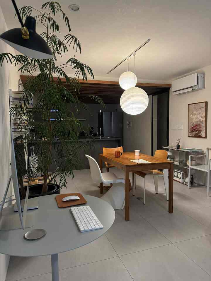 Natural modern dining room with white walls and gray floor, featuring wood-tone dining table, pendant lights, and a minimalist home office desk setup