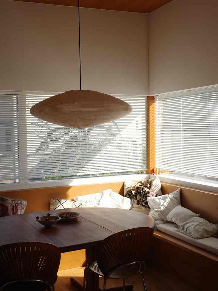 ナチュラルな木目調と白いブラインドのコーナー窓が特徴的なダイニング、造作のベンチとペンダントライトが配置された雰囲気のあるインテリア