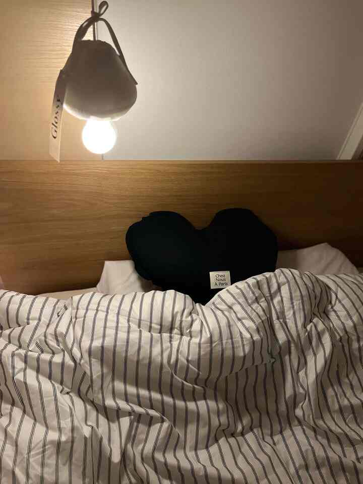 Natural toned bedroom featuring striped bedding, a black heart pillow, and a glowing round lamp creating a cozy atmosphere