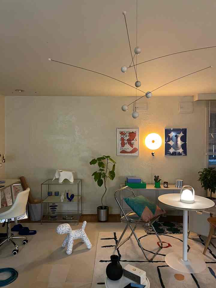 柔らかなベージュの壁と木製フロアを持つ二人暮らしのリビング、北欧スタイルの家具とペット用おもちゃ、間接照明が配置された印象的な空間