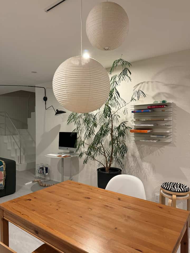 白と茶色の色調のダイニングルーム、大きな吊り下げペンダントライト、木製ダイニングテーブル、白い椅子が配置されたミニマルで自然を感じるインテリア