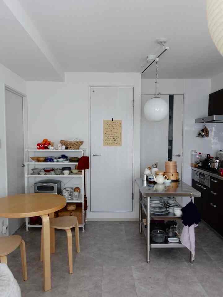 White and light gray toned kitchen featuring a stainless steel kitchen island, wooden dining table, and stools in a clean modern space