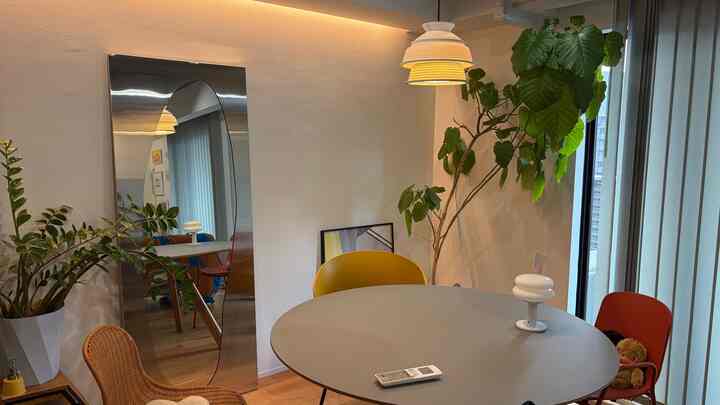 Modern living room featuring a round dining table with yellow pendant light, large stainless steel mirror and plants creating a spacious cozy atmosphere