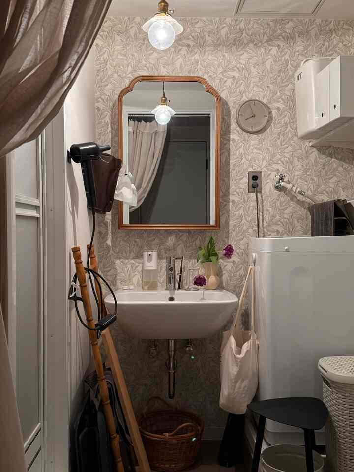 ナチュラルカラーの狭いバスルーム、ベージュの壁紙に洗面台と洗濯機、鏡が配置された効率的な収納空間