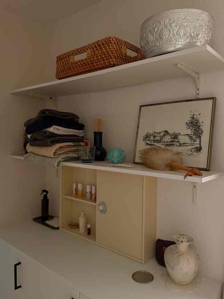 落ち着いたベージュとホワイトの色調の収納スペース、棚には整理ボックスや額縁、ディフューザーが配置された雰囲気のあるインテリア