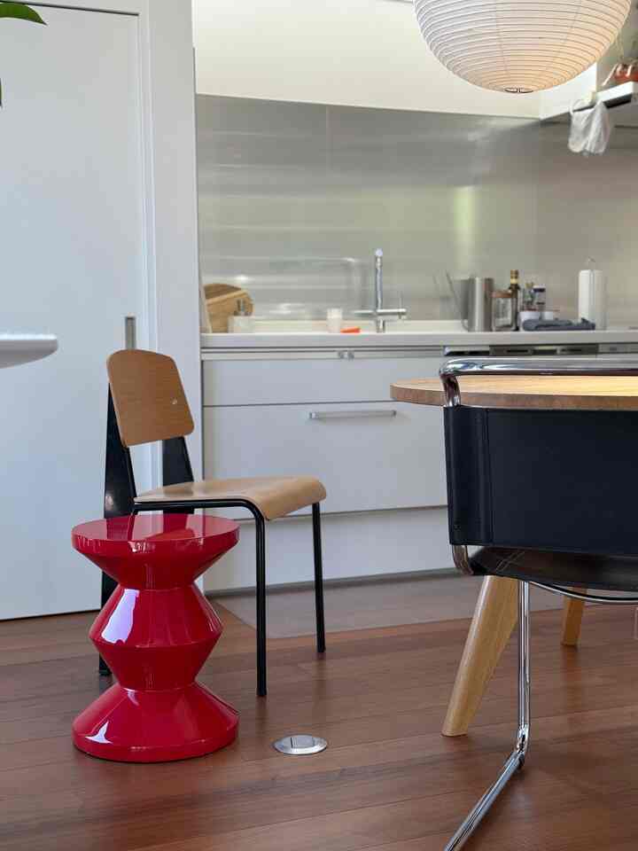 Mid-century modern kitchen dining room featuring a red Zig Zag stool and wooden chairs with a clean, natural atmosphere