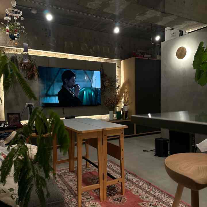 Natural tone studio apartment living room featuring large TV, gray sofa, and wooden dining table creating a cozy atmosphere