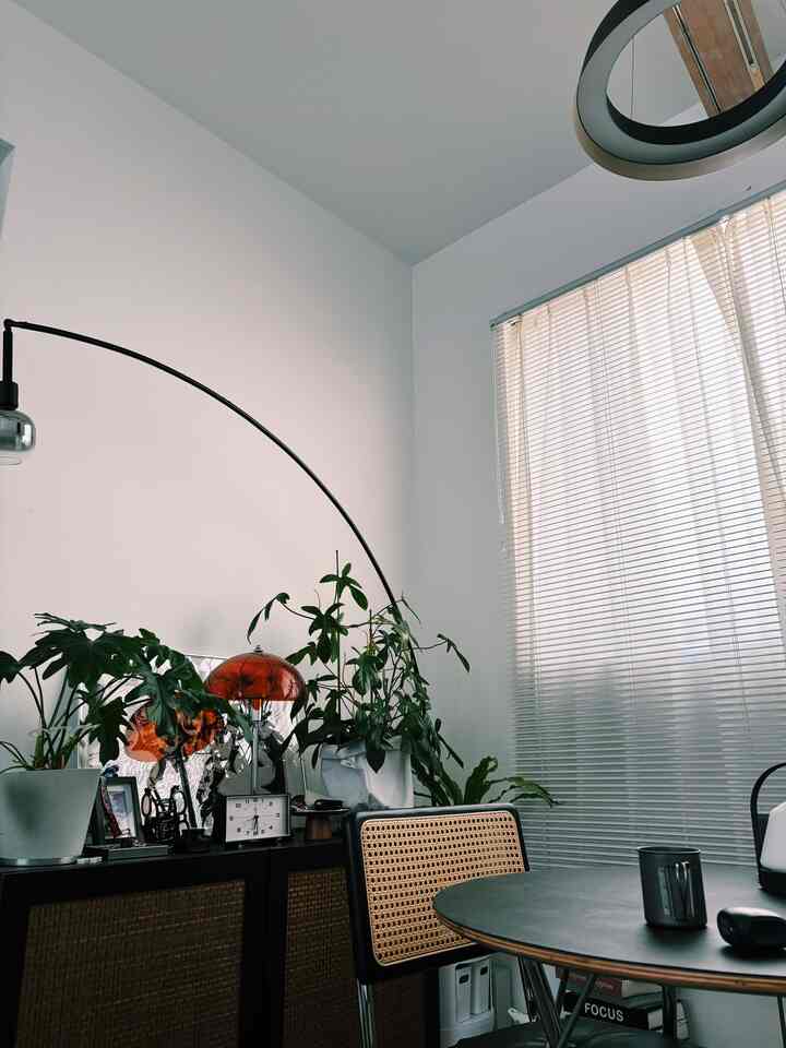 モノトーン調の北欧風ホームオフィス空間、ラタンチェアと丸いダイニングテーブル、アーチ型のフロアランプが配置されたシンプルなインテリア