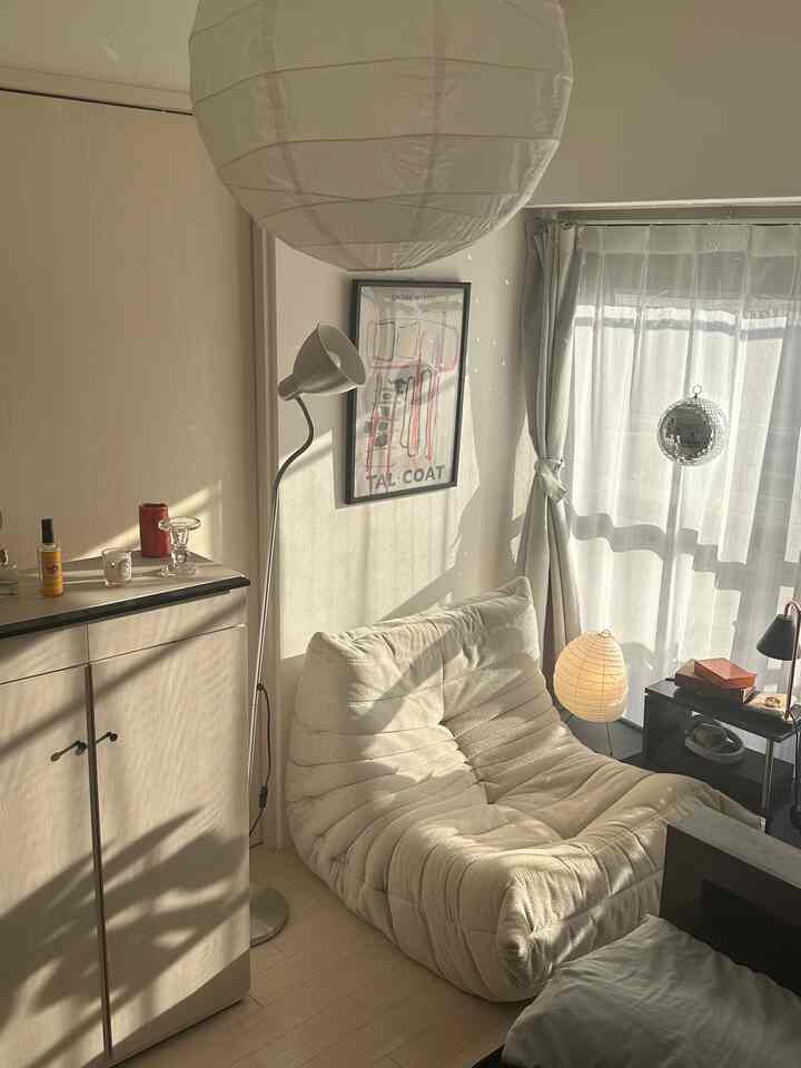 ホワイトとナチュラルカラーの狭いワンルームリビング、快適なソファとペンダントライトが配置されたシンプルでモダンなインテリア