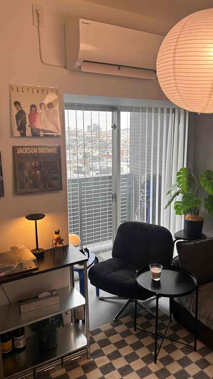 白と黒の色調の6畳の部屋、モダンなアームチェアとサイドテーブル、チェッカーフラッグのラグとブラインドが配置された雰囲気のあるインテリア