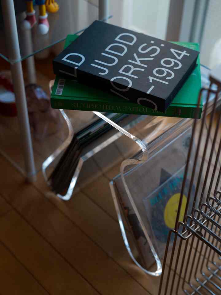 ナチュラルな木目調の床に透明アクリル製のモダンなスツール兼書棚が配置されたシンプルな一人暮らし空間