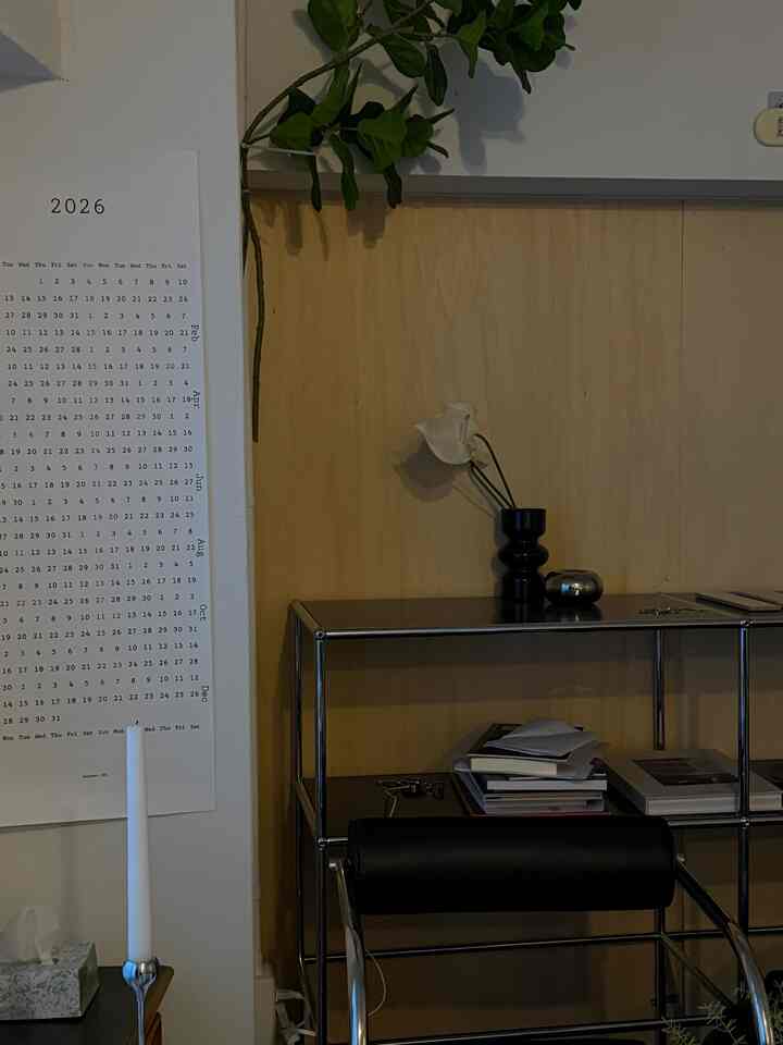 ナチュラルトーンの背景にモダンな黒のレザー椅子と金属製棚が配置されたホームオフィスの雰囲気ある空間