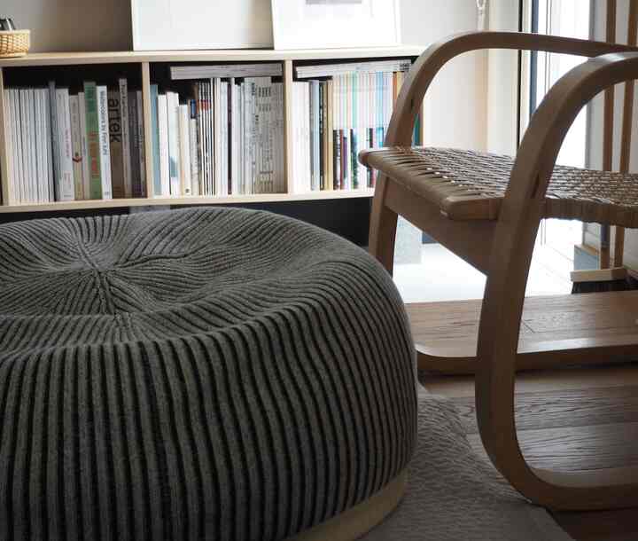 ナチュラルカラーのリビング、グレーのビーズクッションと木製アームチェア、本棚が配置された落ち着いた空間