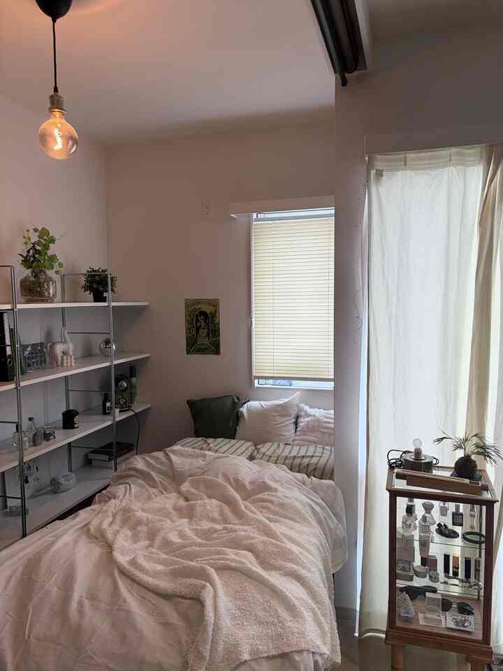 白とベージュを基調とした1LDKの寝室、IKEAの棚やカーテン、ベッドが配置された落ち着いたインテリア