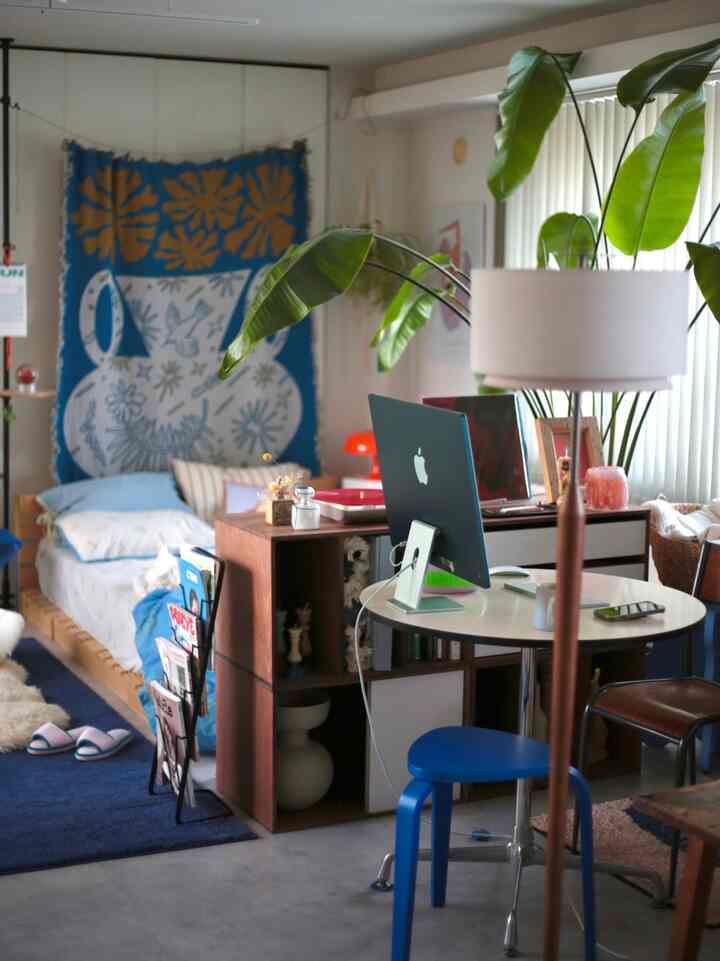 青と茶色の色調のリビング兼寝室、デスクとスツールが配置された自然な雰囲気のホームオフィス空間