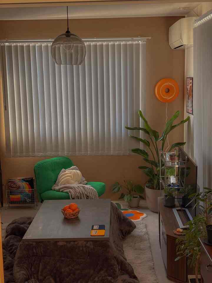 Beige-toned living room with gray kotatsu table, green armchair, and orange wall decor creating a cozy 8-tatami space