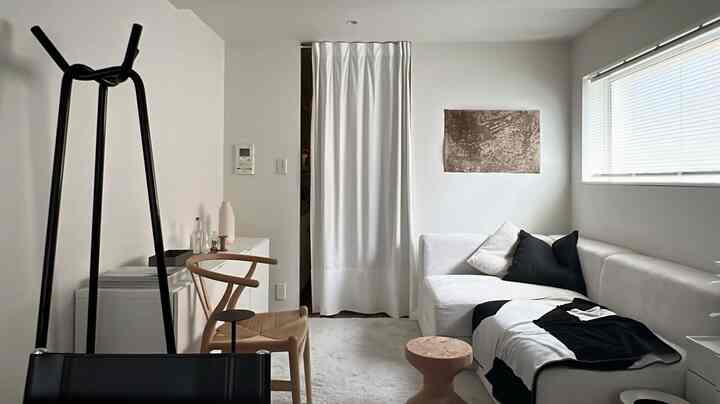 白と木目調が調和したジャパンディスタイルのリビング、コーナーソファとYチェア、カーテンが配置された印象的な空間