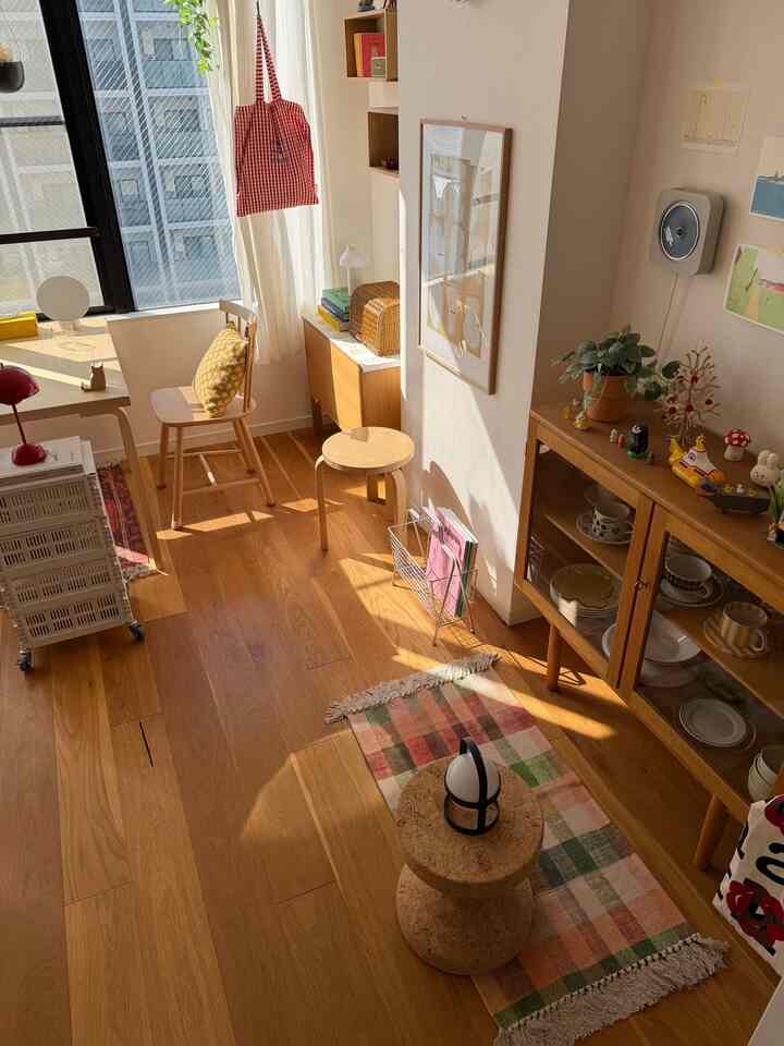 Warm natural-toned single household living space featuring wooden furniture, small stool, desk, and rug with bright and cozy atmosphere