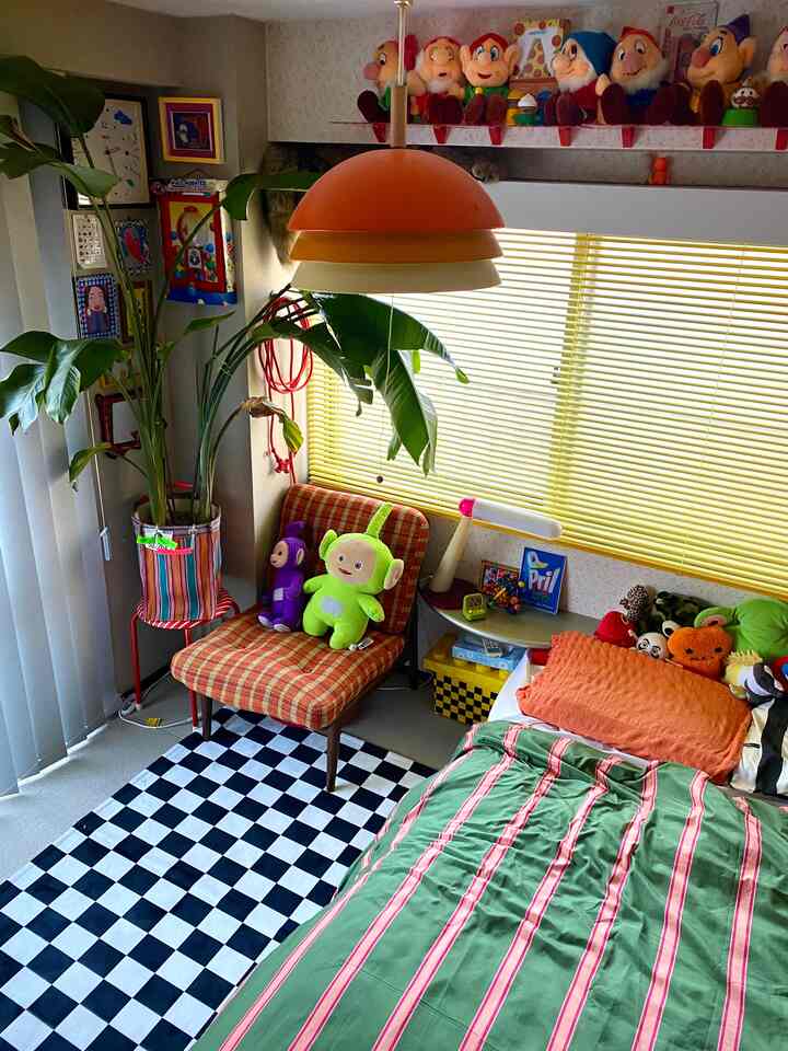 Orange and green toned bedroom featuring a checkerboard rug, vintage armchair, numerous toys, and leafy plants creating a cozy space