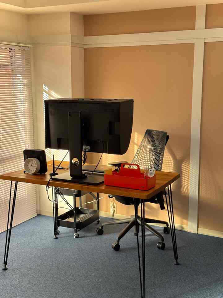 温かみのあるブラウンの壁と木目調のデスクが印象的なレトロなワークスペース、オレンジ色のデスクオーガナイザーとモニター、オフィスチェアが配置された空間