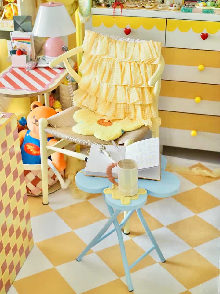 明るい黄色と白の色調の子供部屋、フリルクッションのアームチェアと花形のサイドテーブルが配置されたかわいいインテリア