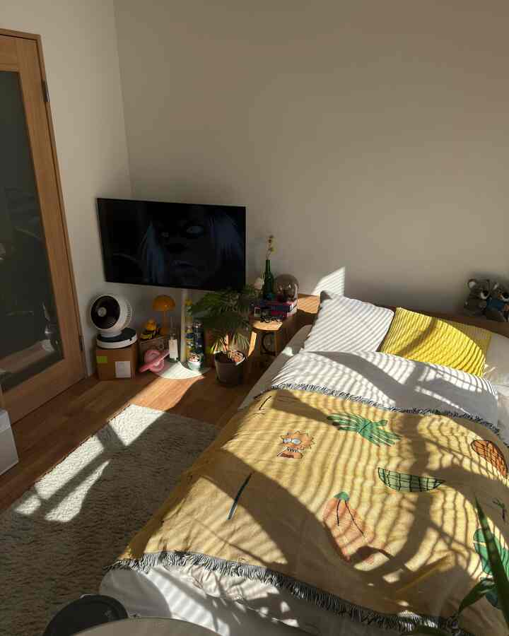 温かみのある木目調と黄色が映える1K寝室、ベッド、スツール、テーブルランプが配置された雰囲気のある空間