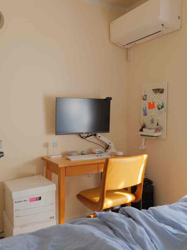 ベージュの壁が印象的なワンルーム、木製デスクと黄色いオフィスチェアが配置された落ち着いたホームオフィス空間