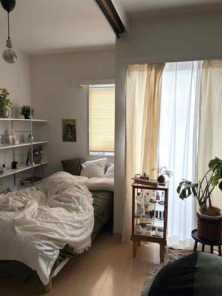 ナチュラルな色調の1LDK寝室とベランダ、白い寝具と植物が配置された雰囲気のあるインテリア