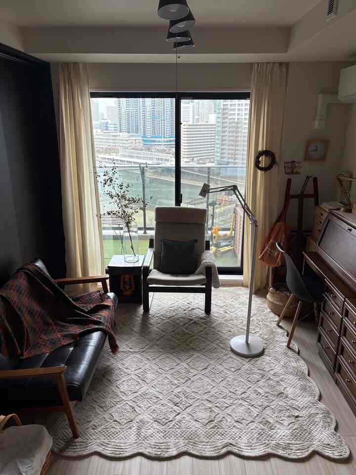 ナチュラルな色調のリビング、広いバルコニー窓とアイボリーのラグ、木製家具が配置された居心地の良い空間