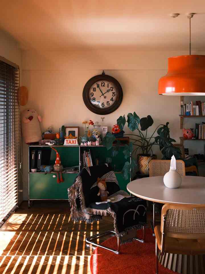 温かみのあるオレンジとグリーンの色調が調和したダイニング、ブラインドの影が床や壁に映る雰囲気のあるインテリア