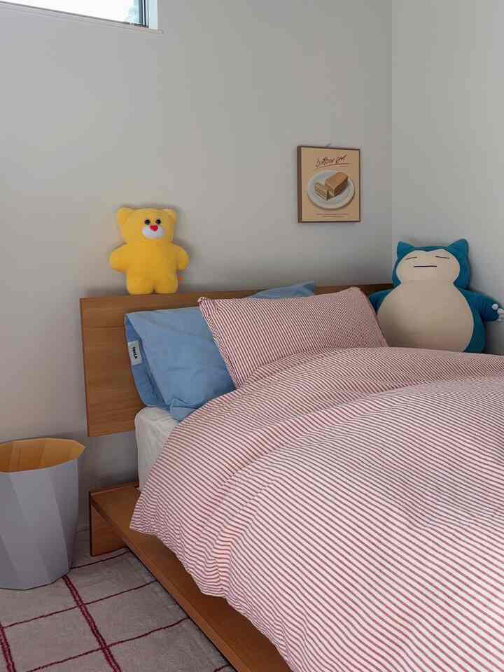 赤いストライプの寝具と青い枕がある子供部屋、黄色と青のぬいぐるみが配置された印象的な空間