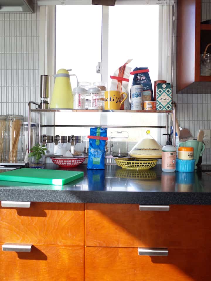 温かみのある木目調の収納があるキッチン、さまざまな調理器具と黄色のケトル、緑のまな板が配置された整然とした空間