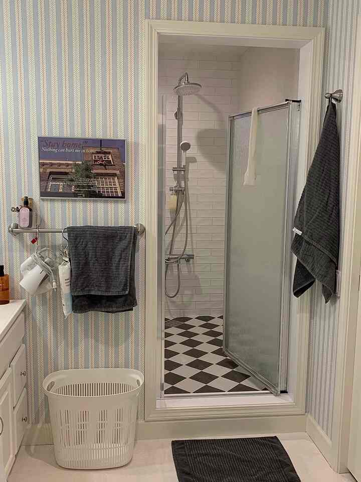 白と黒のモノトーンのバスルーム、タイル床とタオル、ポスターが配置された印象的な空間