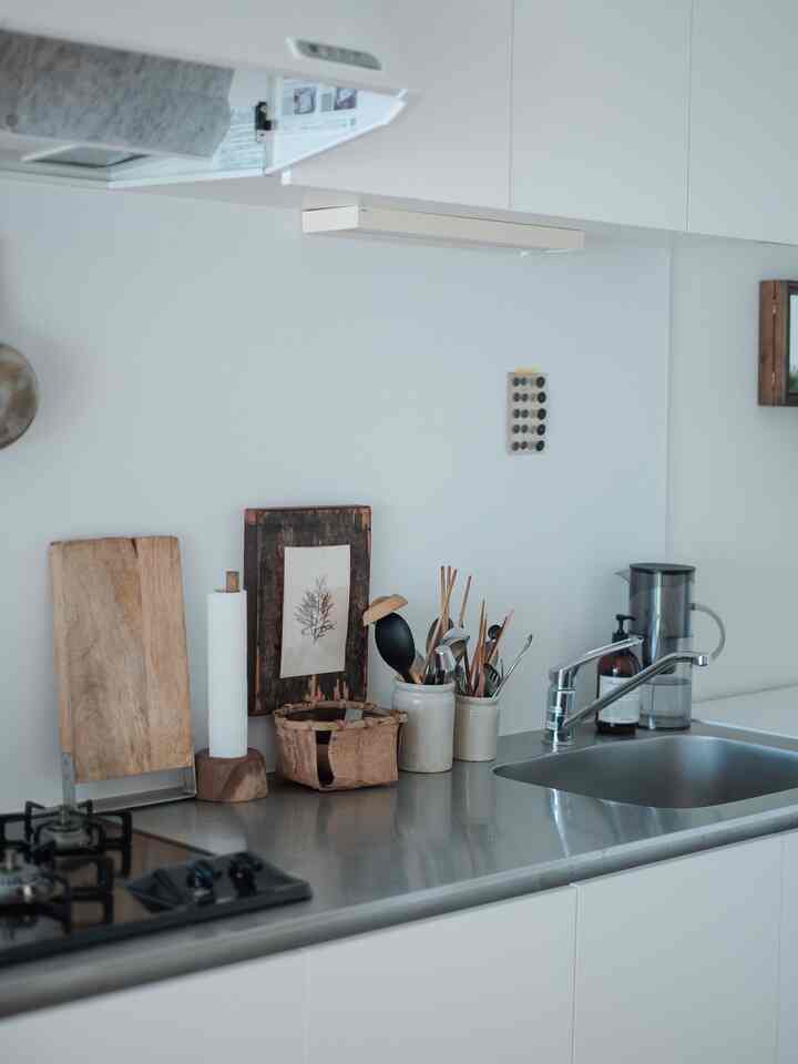 ホワイトとナチュラルトーンのキッチン、ステンレスのカウンター上にまな板と調理器具が整頓された清潔感のある空間