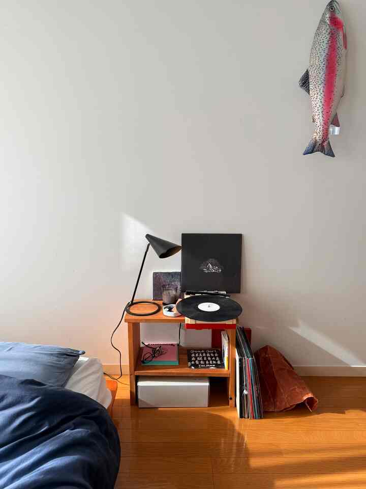 Warm brown wooden floor and navy bedding in a studio apartment bedroom featuring a small wooden side table with a record player, cozy atmosphere