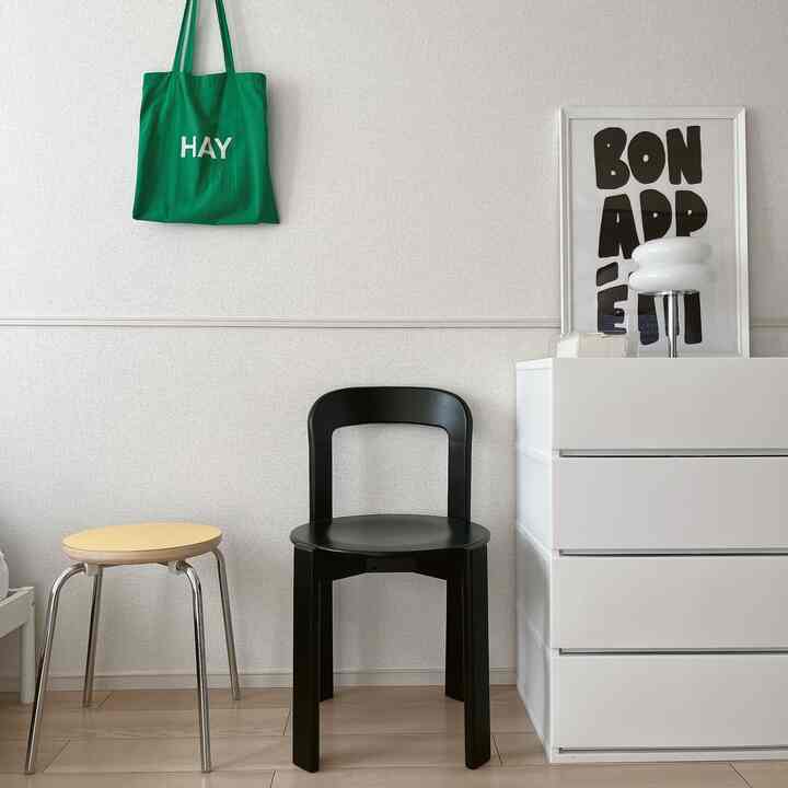 Minimal Korean interior space featuring white walls and dresser, a black dining chair, and a yellow stool