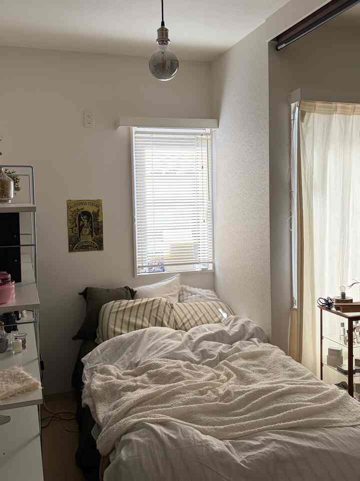 白とベージュのトーンが調和する1LDKの寝室、整えられたベッドとブラインドが印象的な落ち着いた空間