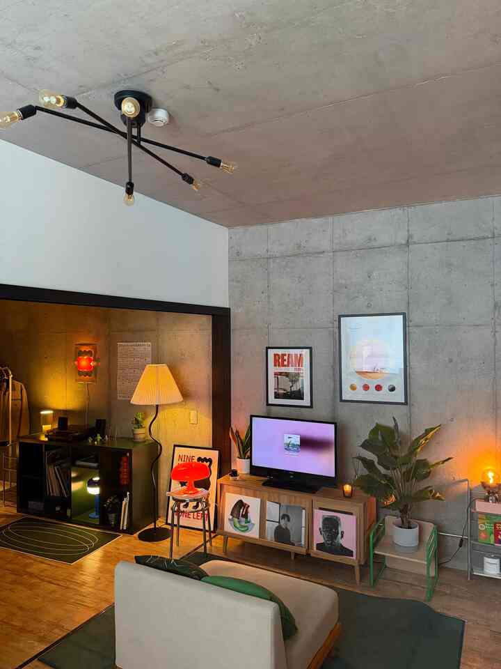 A modern living room featuring natural wood tones and concrete walls, with floor lamps and art posters creating a cozy atmosphere