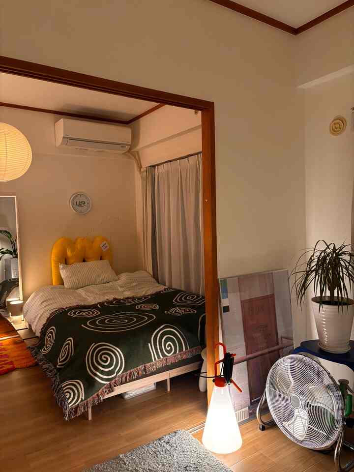 温かみのあるベージュと木目調の寝室、黄色いクッションヘッドボードと緑の模様入りブランケットがあるミッドセンチュリーモダンな印象的な空間