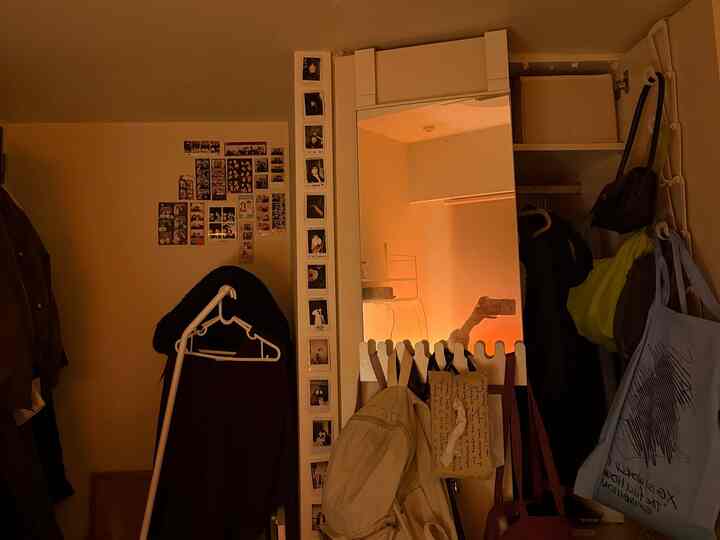 ダークブラウンとベージュのトーンが特徴的な狭い玄関空間に、コートラックと大きな鏡が配置され、散らかった雰囲気のあるインテリア