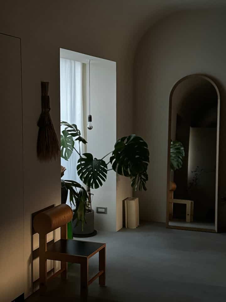 柔らかなモノトーンとグリーン植物が調和するモダンな玄関、アールデコのアーチ天井とゴールドトーンのスツールが置かれた落ち着いた空間