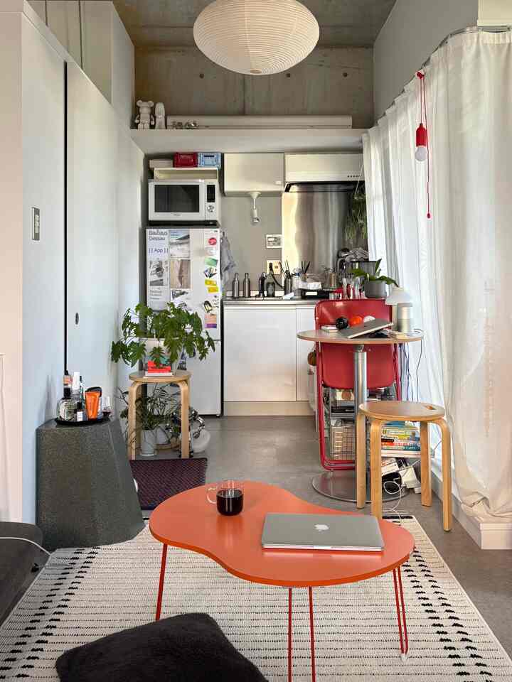 Natural tones with red accents in a studio living room featuring an orange folding table and compact kitchen in a cozy space