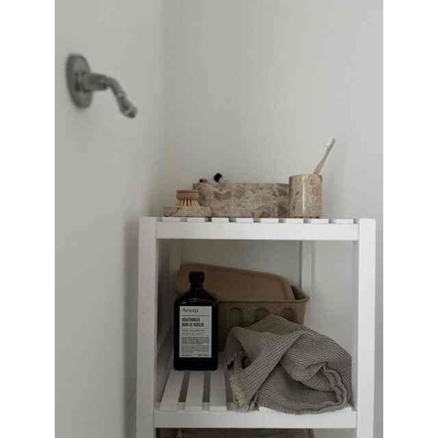 ホワイトとベージュの色調のバスルーム、白い棚に浴室用品とタオルが整頓された印象的なインテリア