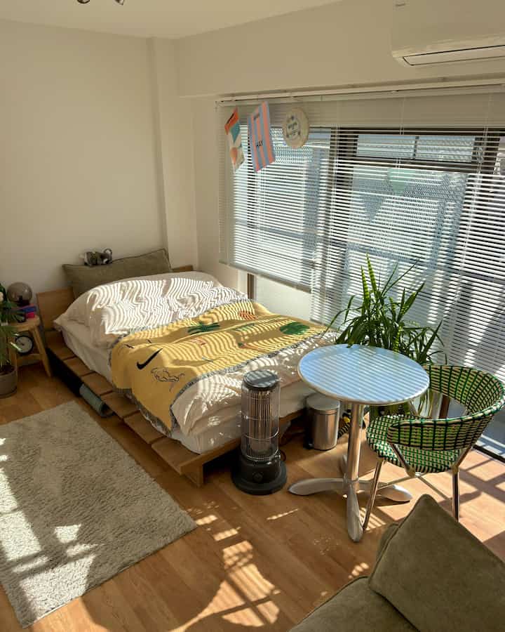 Bright toned bedroom with wood accents, sunlight streaming through window blinds creating a cozy atmosphere