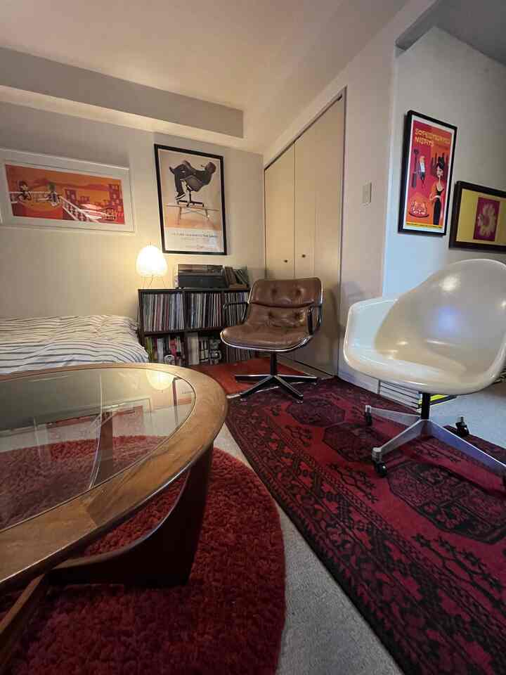 赤いラグ敷きのミッドセンチュリーモダンな寝室兼リビング、アームチェアとテーブルが配置された落ち着いた空間