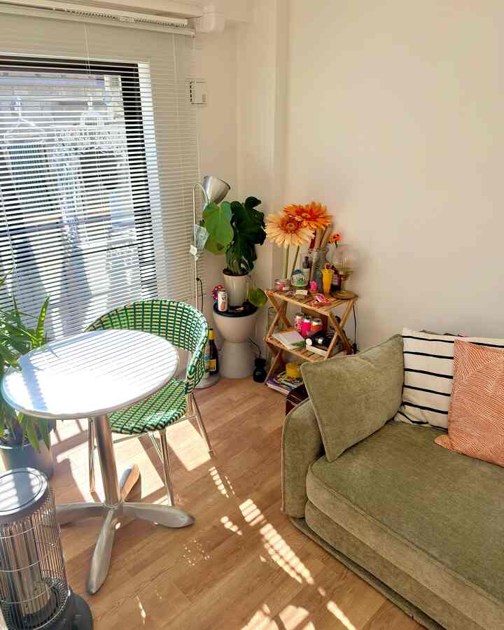 ナチュラルな木目調の床とグリーンのソファベッドが配置された7畳の一人暮らし向けコンパクトな部屋、おうちカフェの雰囲気あるインテリア