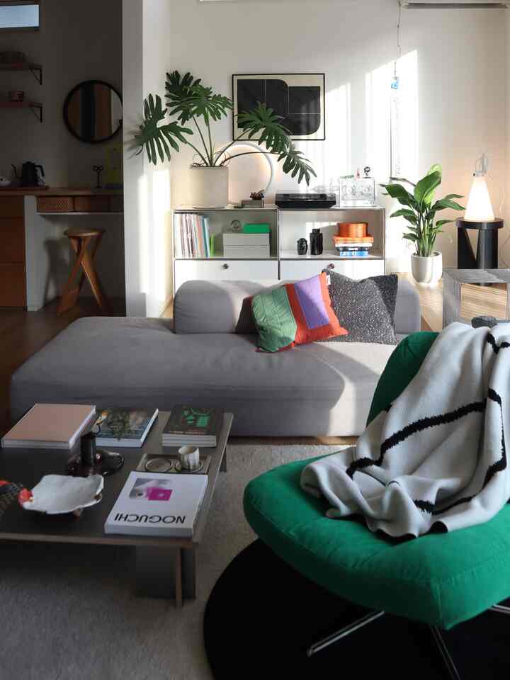 自然光が差し込むナチュラルモダンなリビング、グレーのソファとグリーンのアームチェア、シルバーのコーヒーテーブル、クッション、植物が配置された空間